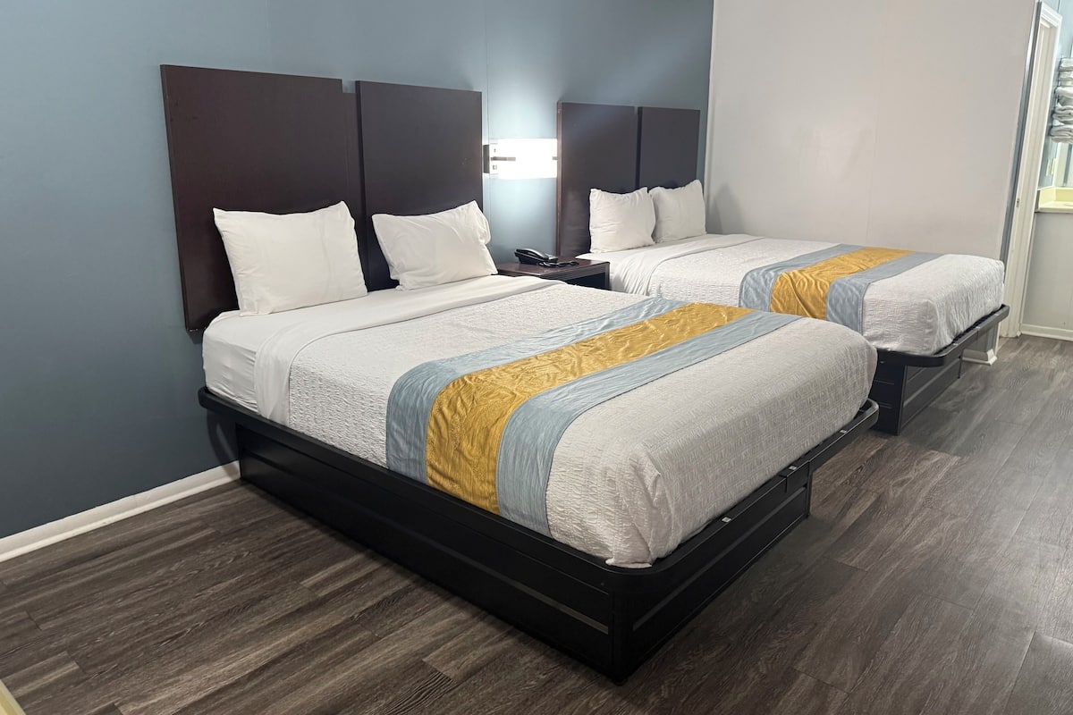 Habitación de hotel con dos camas, piso de madera oscura y diseño moderno.