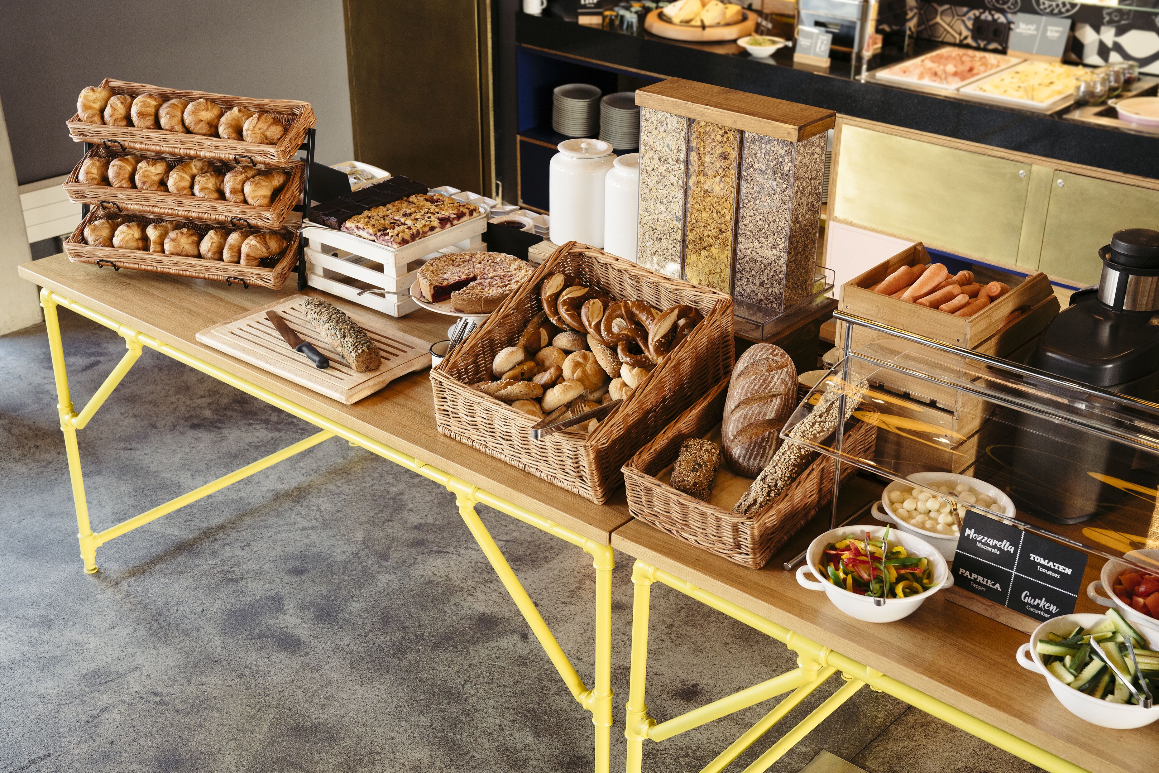 A buffet table with various food items including bread, pastries, and salads.
