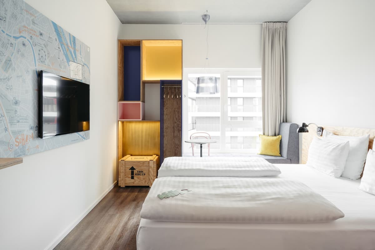 A hotel room with two beds, a map on the wall, a wooden chest, and a window with curtains.