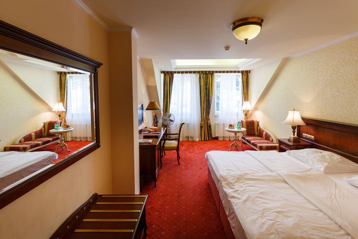 A hotel room with two beds, a desk, a chair, a small table, and a mirror.