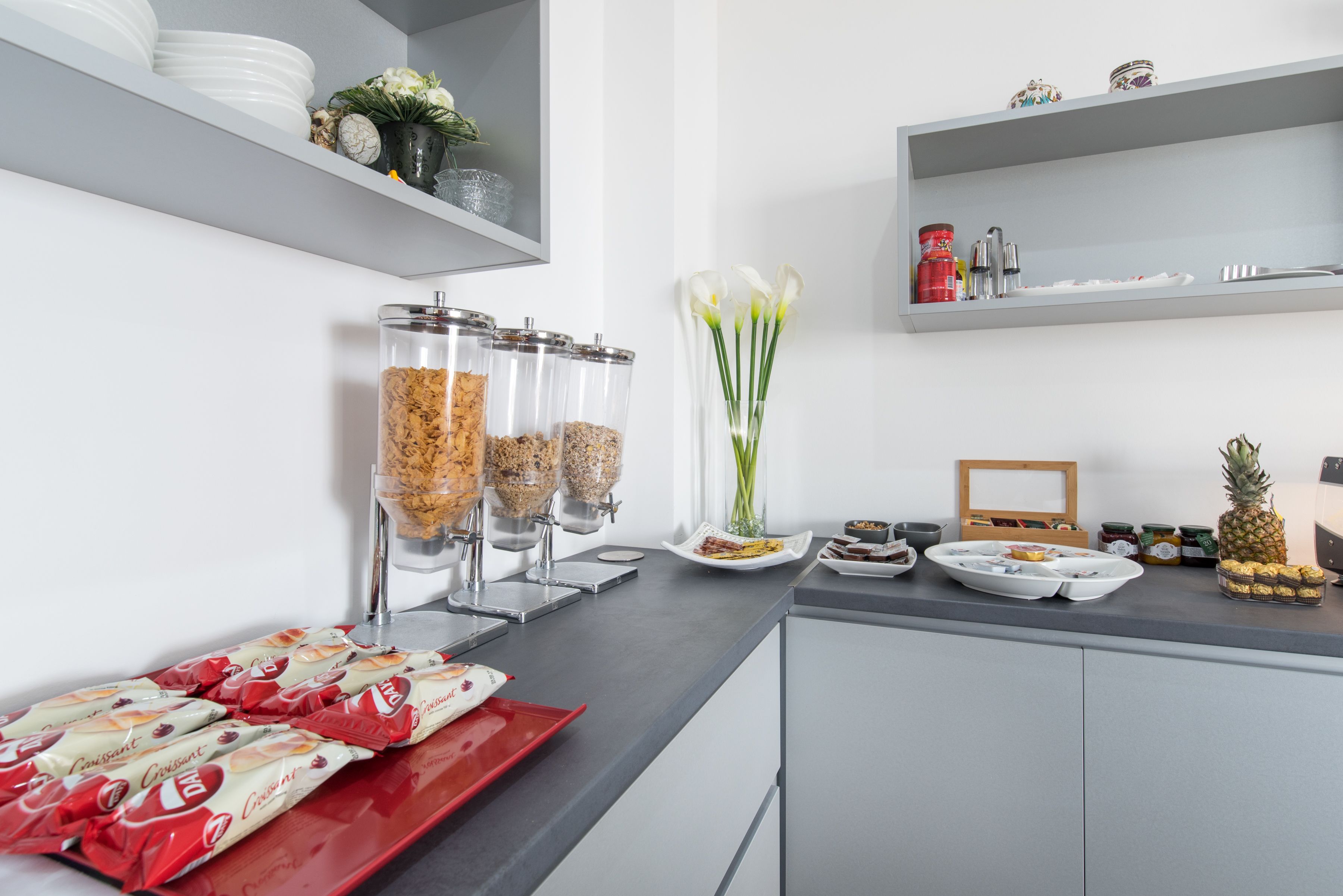 A modern kitchen with a counter displaying food items, a coffee station, and decorative elements like flowers and a pineapple.