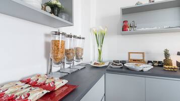 A modern kitchen with a counter displaying food items, a coffee station, and decorative elements like flowers and a pineapple.