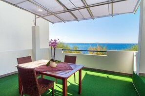 A balcony with a table and chairs, a potted plant, and a view of the sea. - Beachfront Villa Mediteran (Podstrana)
