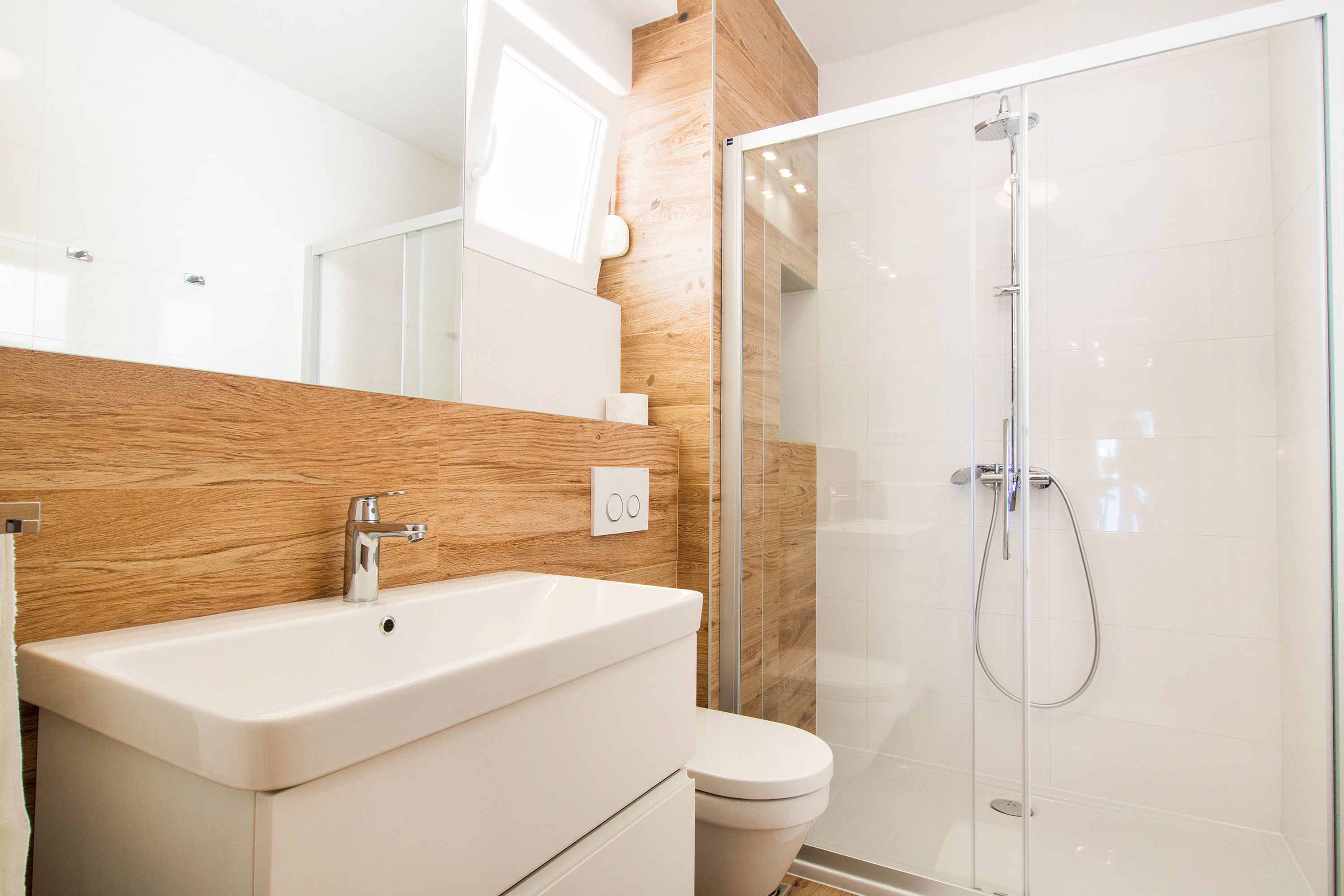Un baño moderno con tocador de madera, cabina de ducha de vidrio y un inodoro blanco.