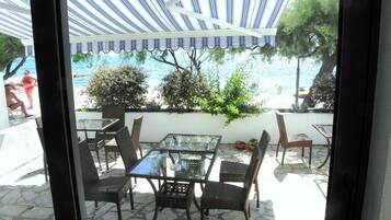 An outdoor patio with a glass table and wicker chairs, overlooking a beach and the sea.
