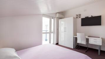 A bedroom with a bed, a desk, a chair, a wardrobe, and a TV mounted on the wall.