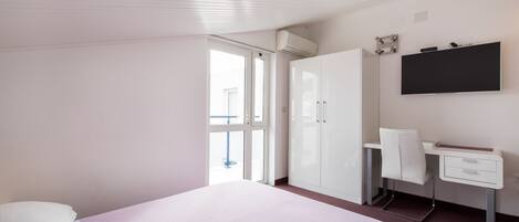 Un dormitorio con cama, escritorio, silla, armario y televisor montado en la pared.