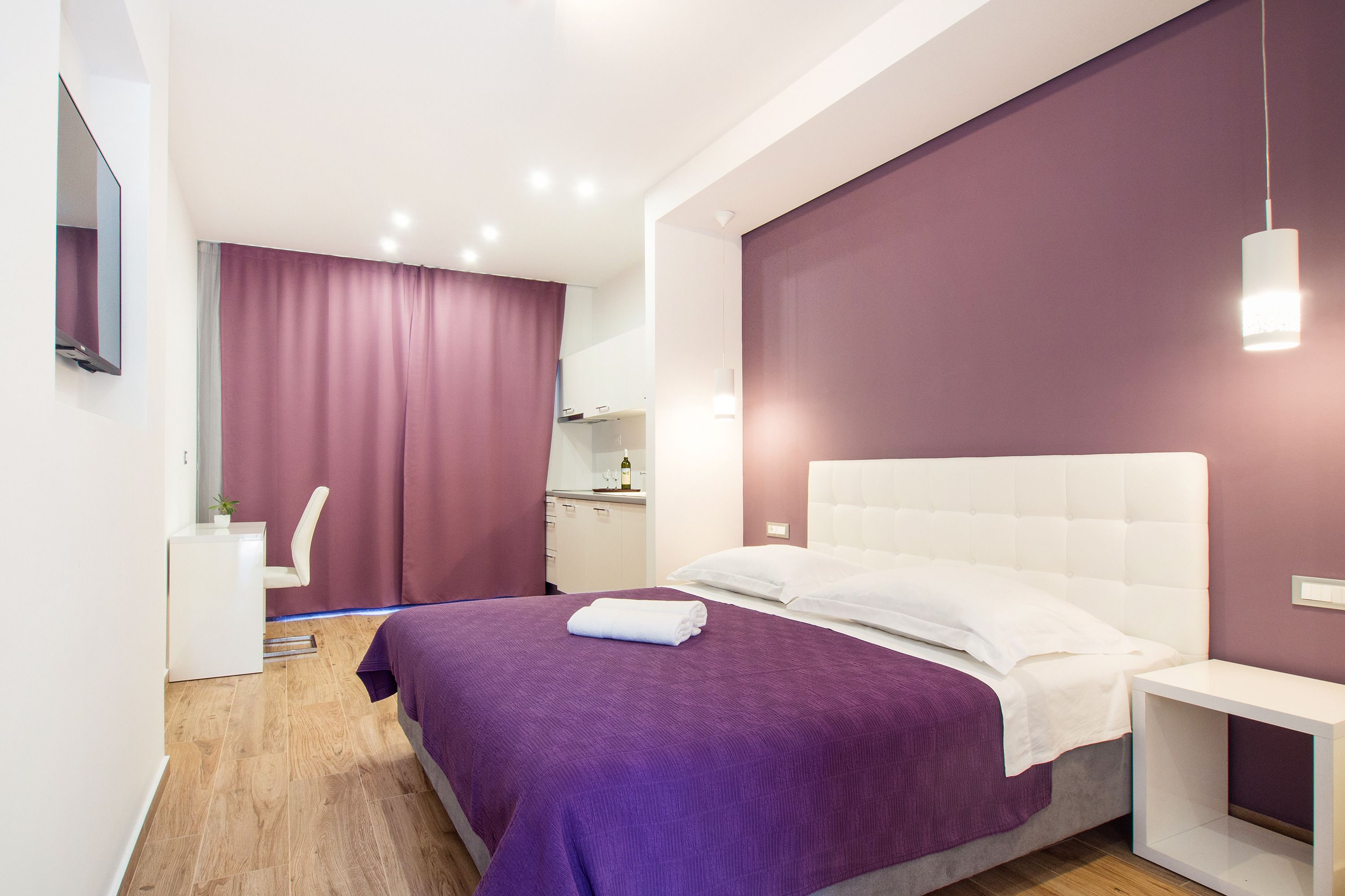 A modern bedroom with a large bed, a bedside table, a desk, and a chair.