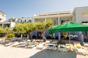 A hotel courtyard with outdoor seating, including white plastic chairs and tables, under a green umbrella. - Beachfront Villa Mediteran (Podstrana)