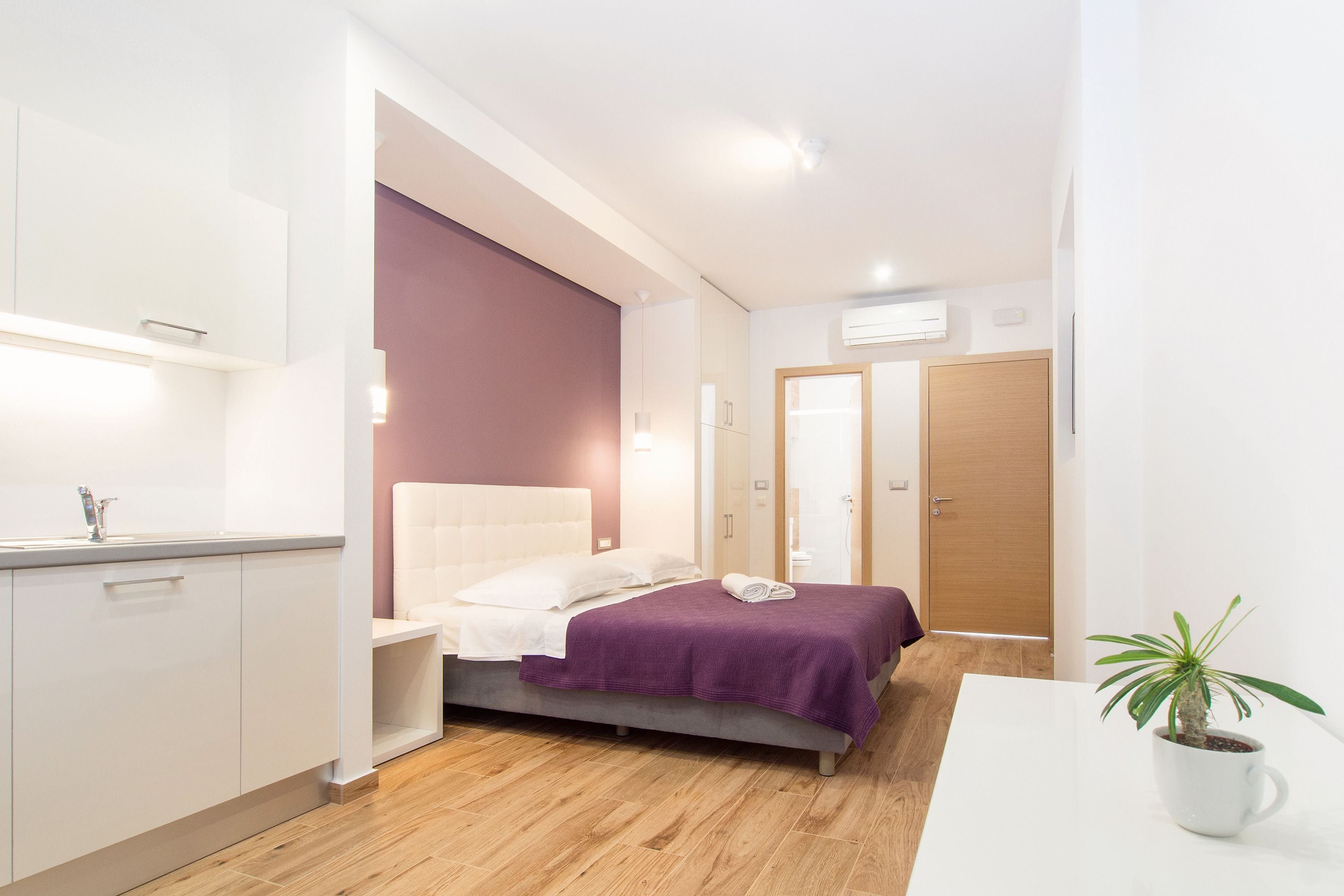 A modern bedroom with a bed, bedside table, and a potted plant.