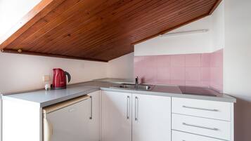 A compact kitchen with white cabinets, a stainless steel sink, and a red kettle.