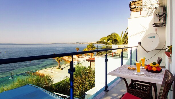 A balcony with a view of the sea, a table with fruits and drinks, and a white wall with a satellite dish. - Beachfront Villa Mediteran (Podstrana)
