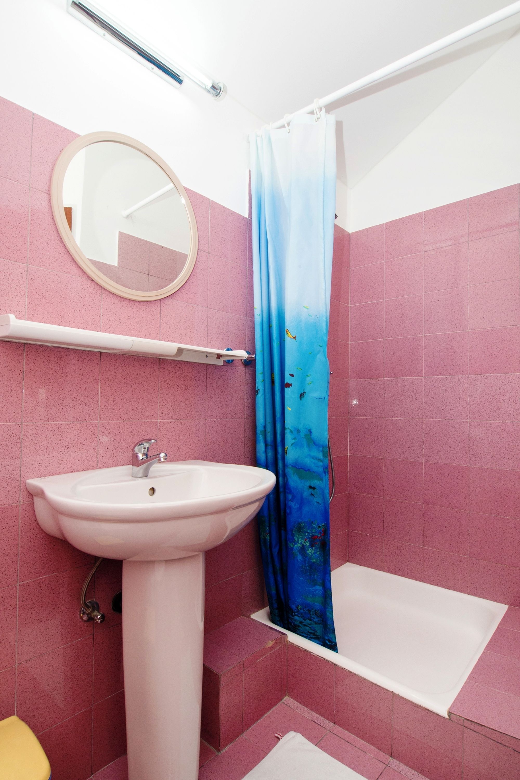 A bathroom with pink tiles, a white sink, a mirror, and a shower curtain.