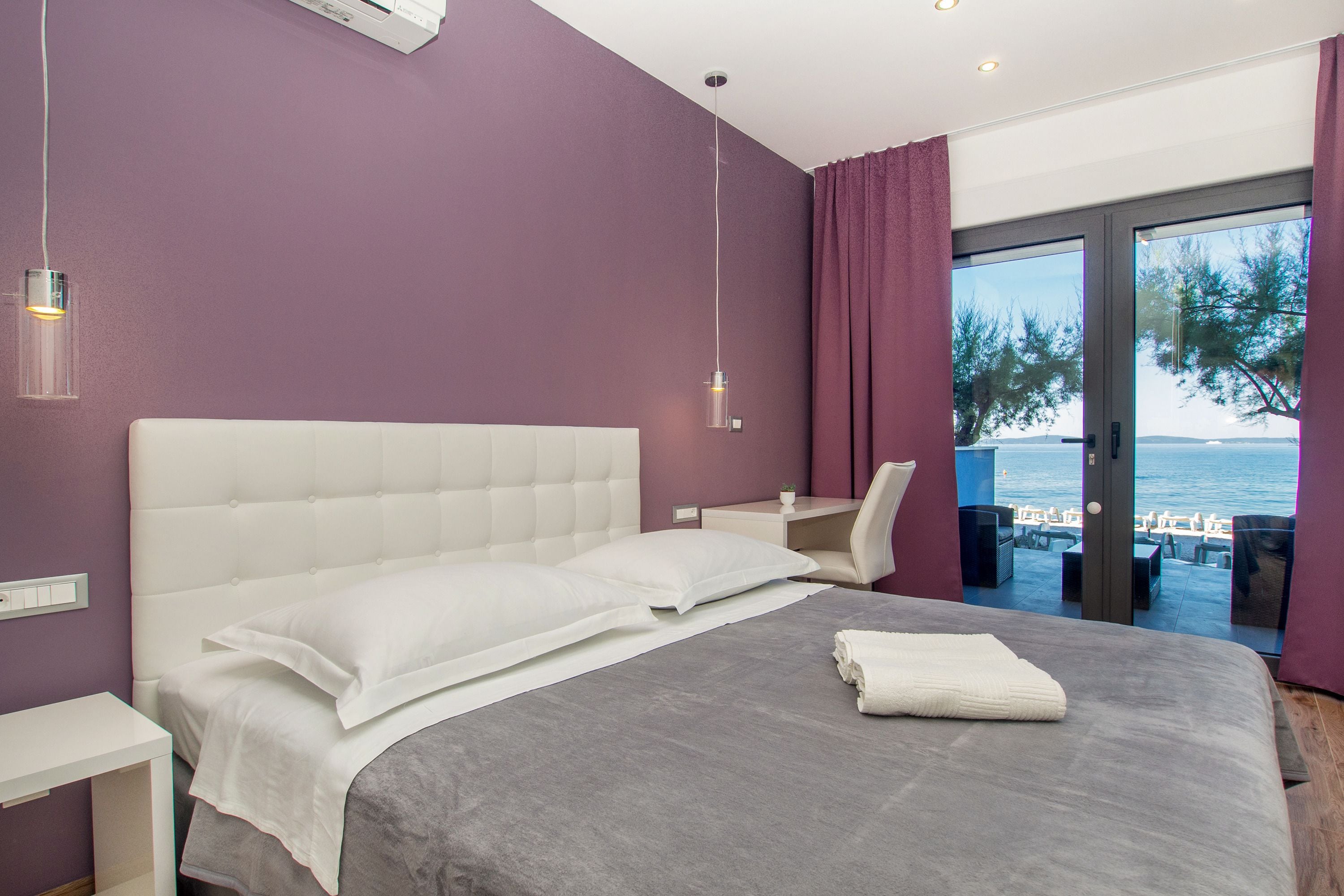 A bedroom with a large bed, a desk, and a view of the sea.