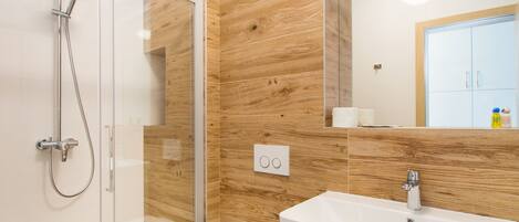 A modern bathroom with a glass-enclosed shower, a white sink, and wooden paneling on the walls.