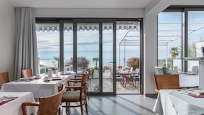 A dining area with tables set for two, large windows with a view of the sea, and a glass door leading to an outdoor patio. - Beachfront Villa Mediteran (Podstrana)