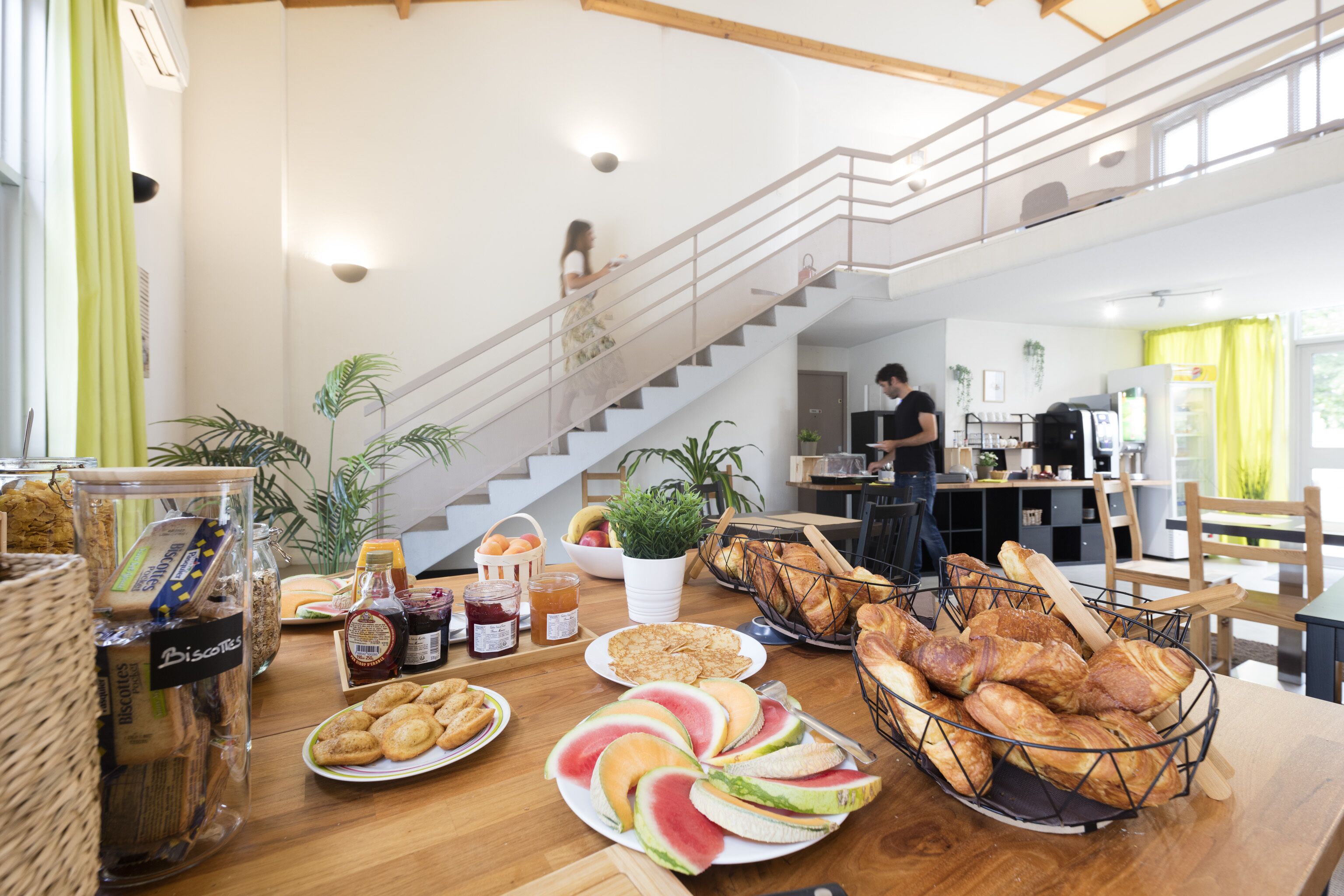 A breakfast buffet with various food items, a staircase, and a kitchen area.