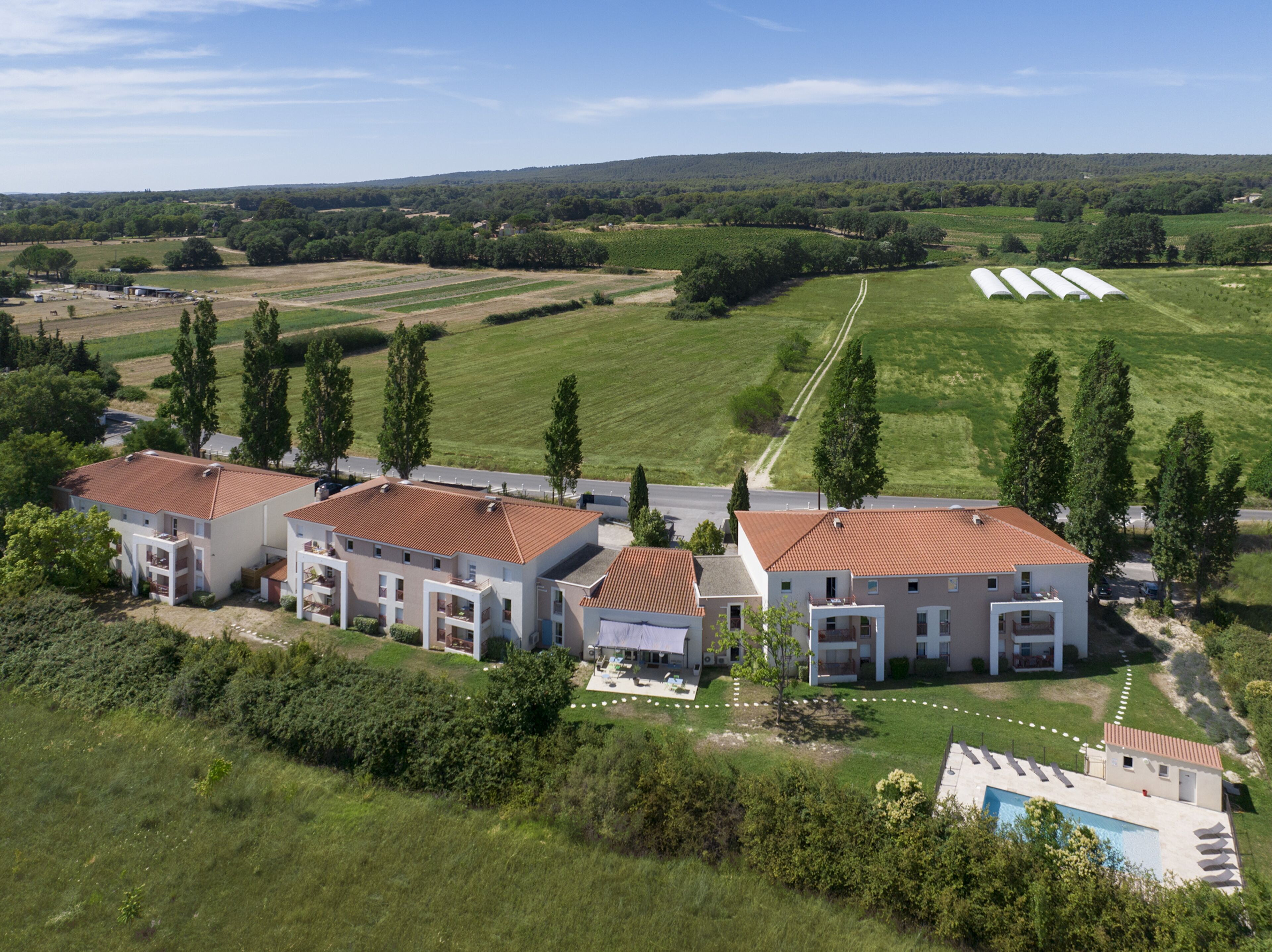 Un quartier résidentiel moderne comprenant plusieurs maisons à deux étages, une piscine et une route traversant le terrain.