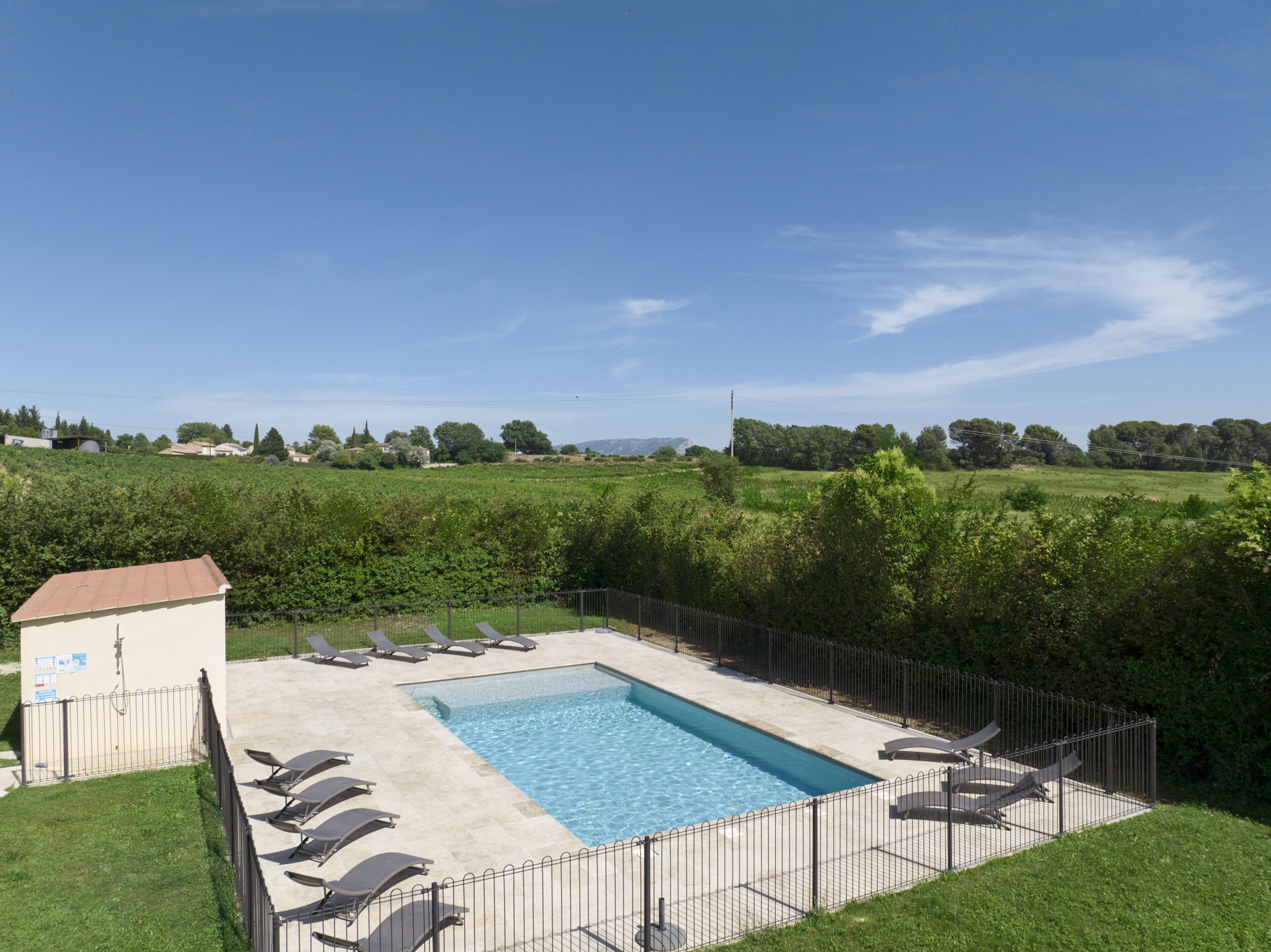 A rectangular swimming pool with a tiled deck, surrounded by a metal fence.