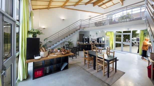 Una cocina amplia con comedor, una escalera que conduce a un nivel superior y grandes ventanales que permiten la entrada de luz natural.