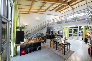 Une cuisine spacieuse avec un coin repas, un escalier menant à l’étage supérieur et de grandes fenêtres qui laissent entrer la lumière naturelle.