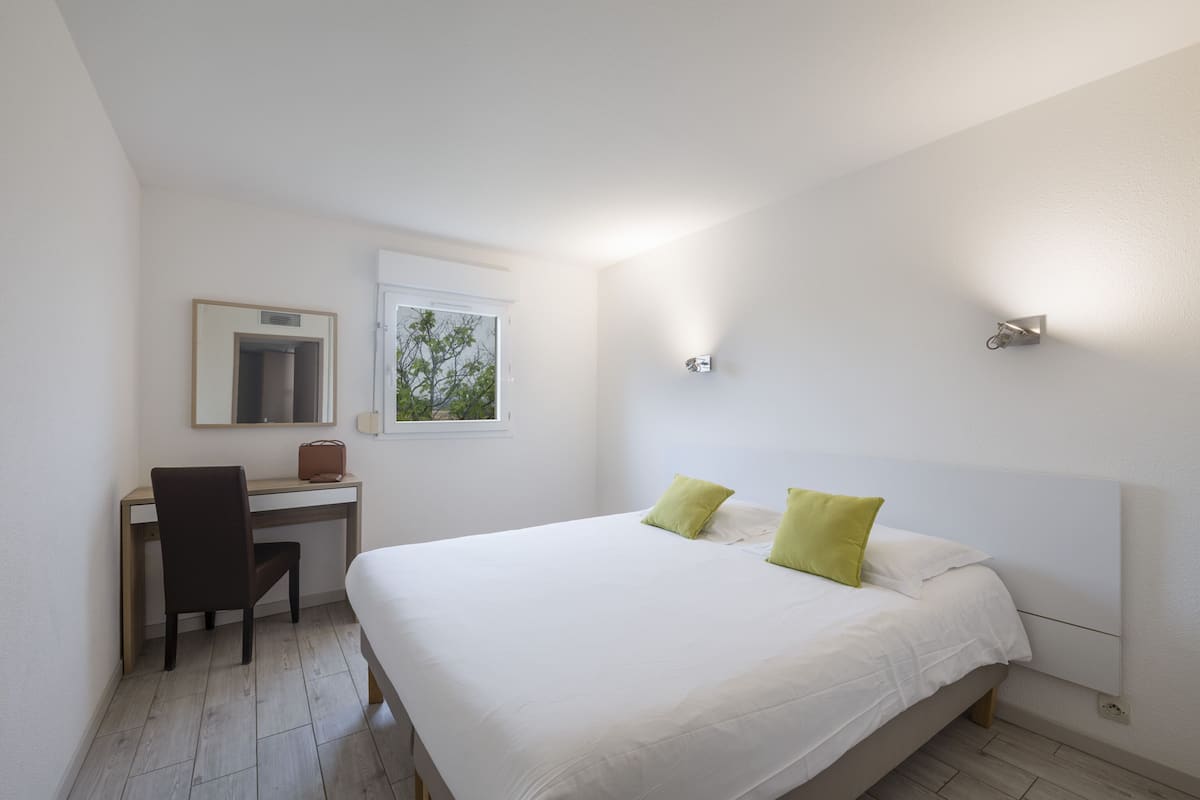 Un dormitorio con cama, escritorio, silla, ventana y espejo.