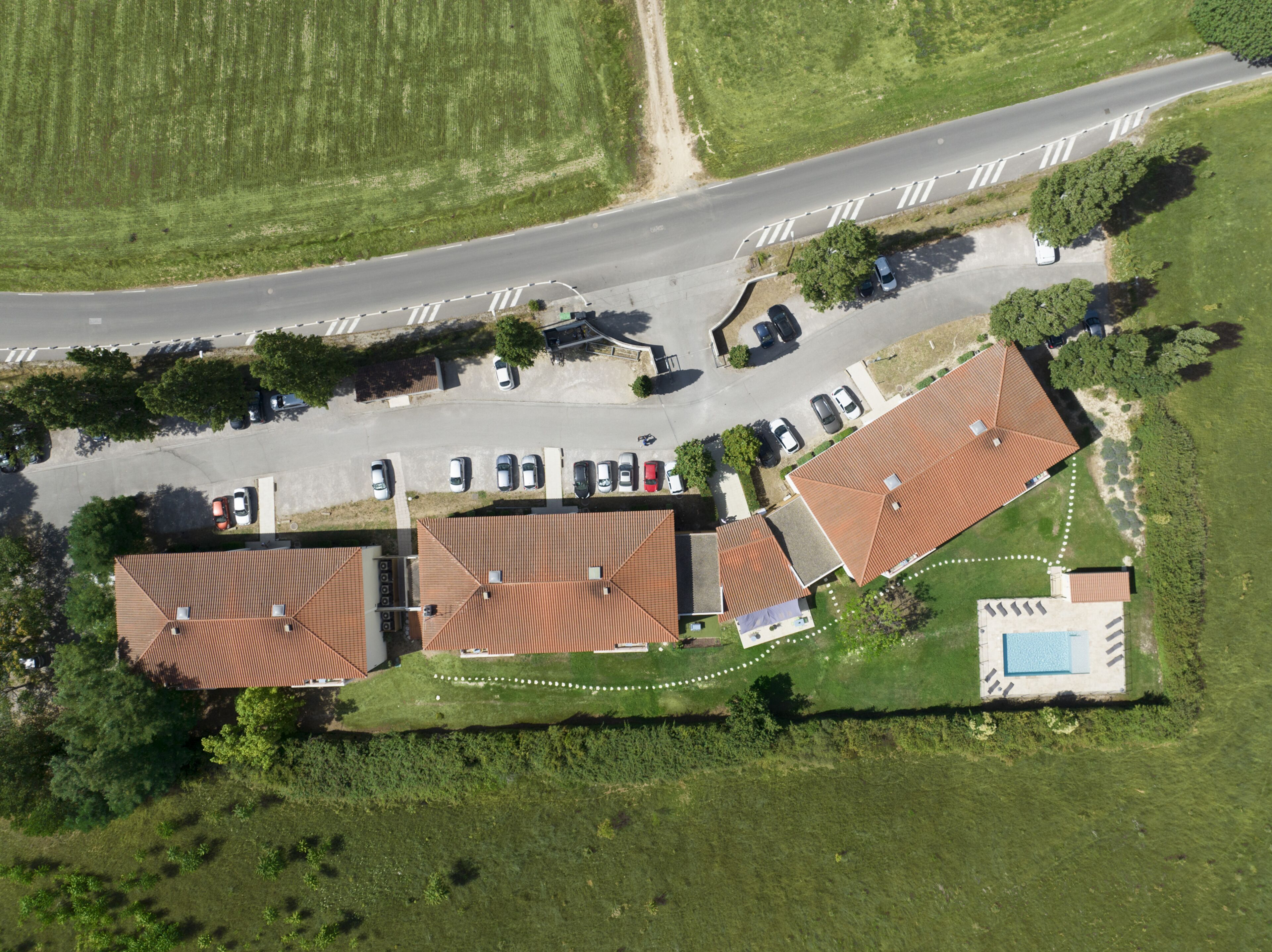 Vista aérea de un área residencial con varias casas, una piscina y una calle con automóviles estacionados.