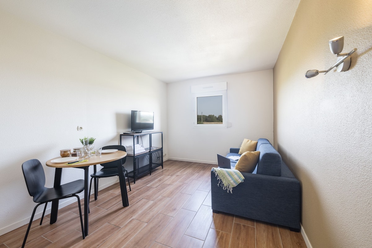 Un espacio habitable compacto con comedor, sofá, televisor y una pequeña mesa con sillas.