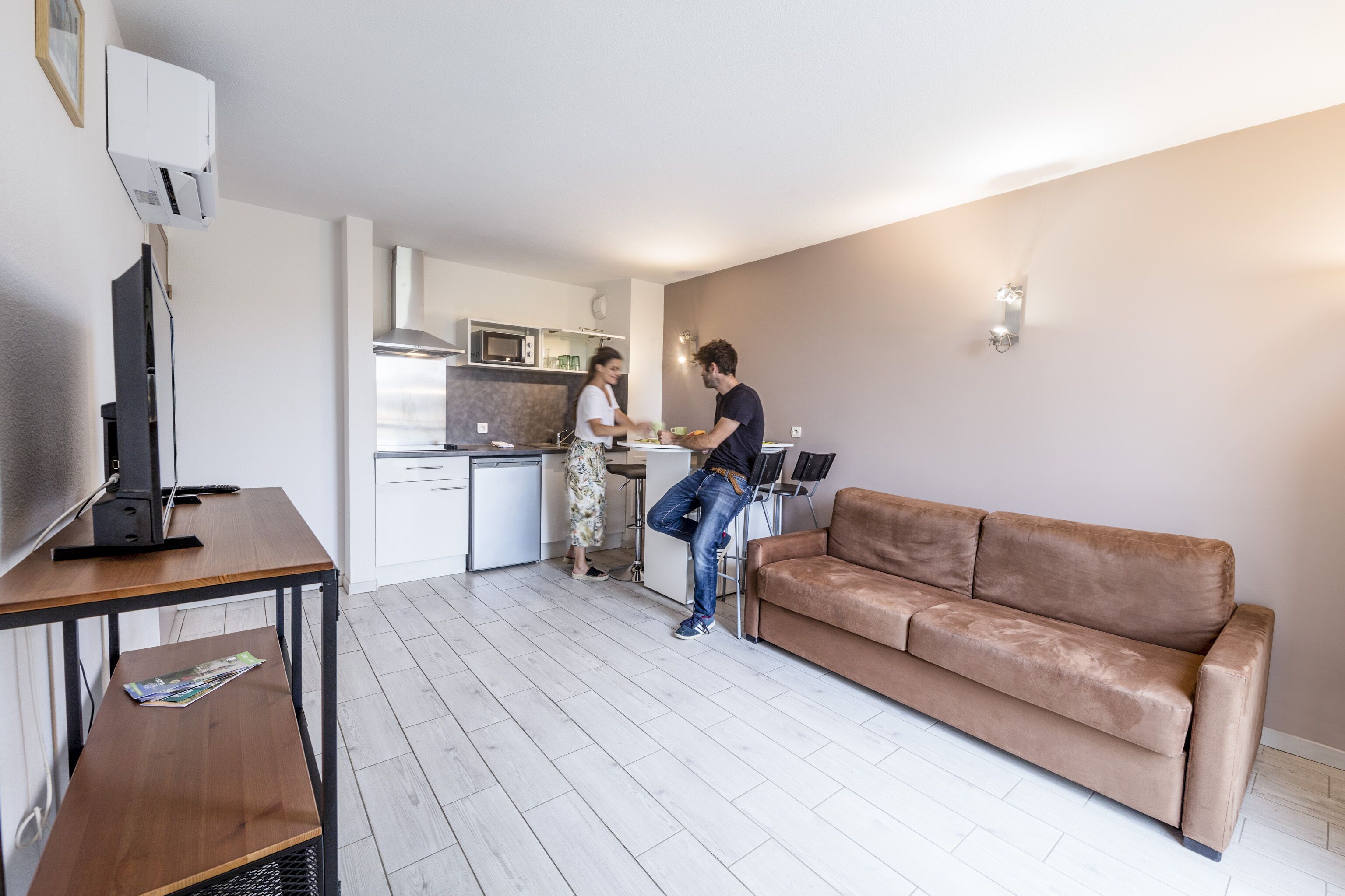 Un salon moderne avec un canapé en cuir marron, une table basse en bois et un téléviseur posé sur un meuble.