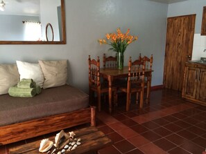 Ein gemütliches Wohnzimmer mit einer Holzsofa, einem Esstisch mit Stühlen, einer Vase mit Blumen und einem Holzschrank.