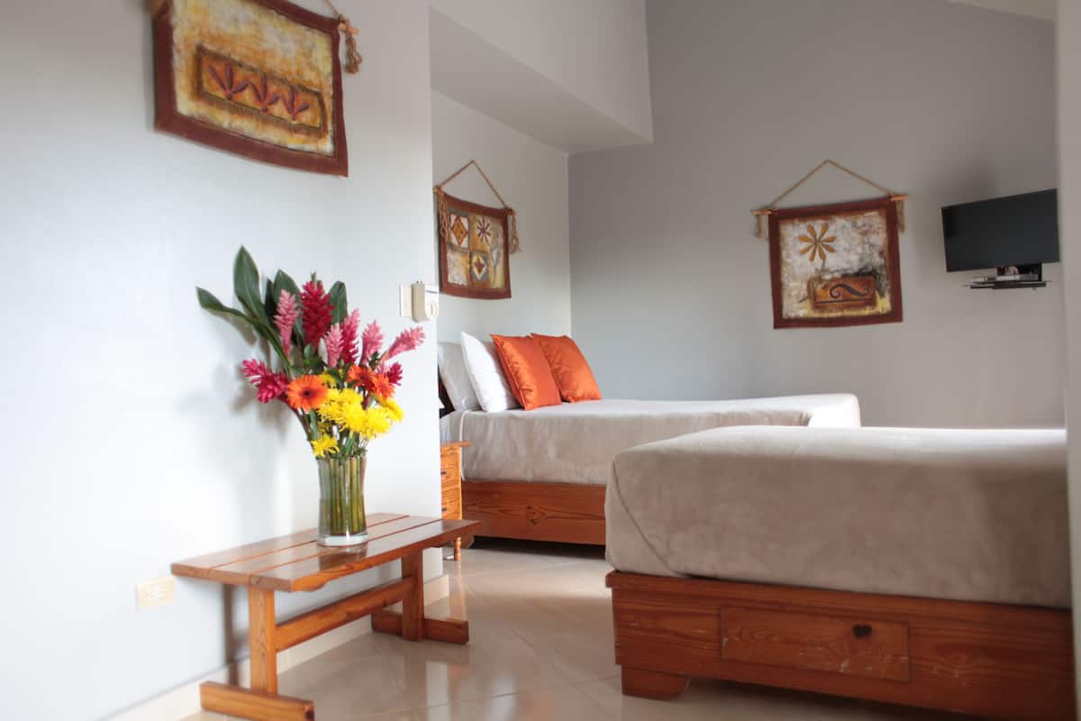 Une chambre avec deux lits, une table de chevet en bois, un téléviseur fixé au mur et des éléments décoratifs accrochés au mur.