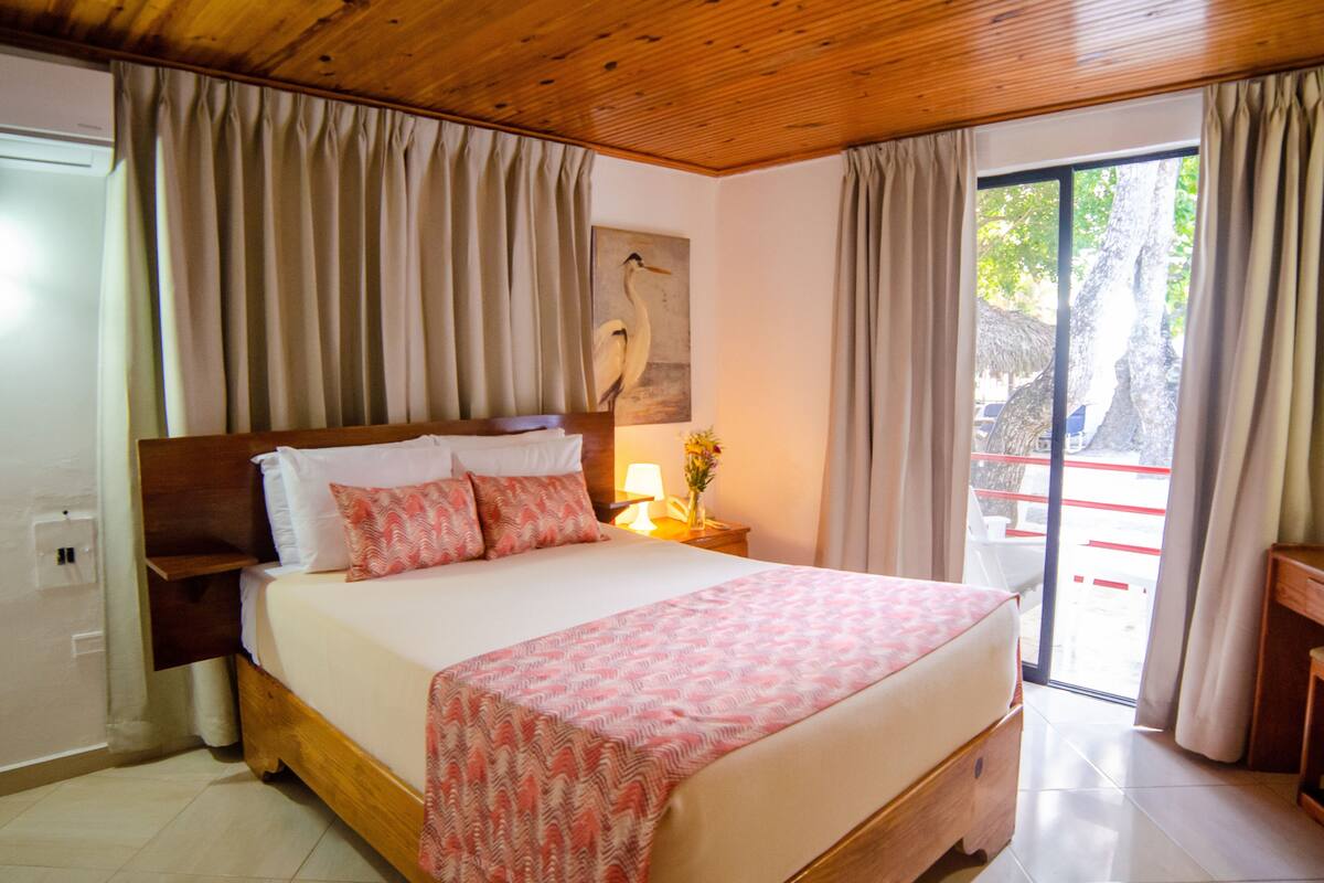 Une chambre d’hôtel avec un grand lit, une table de chevet avec une lampe et une vue sur l’extérieur grâce à une porte coulissante.
