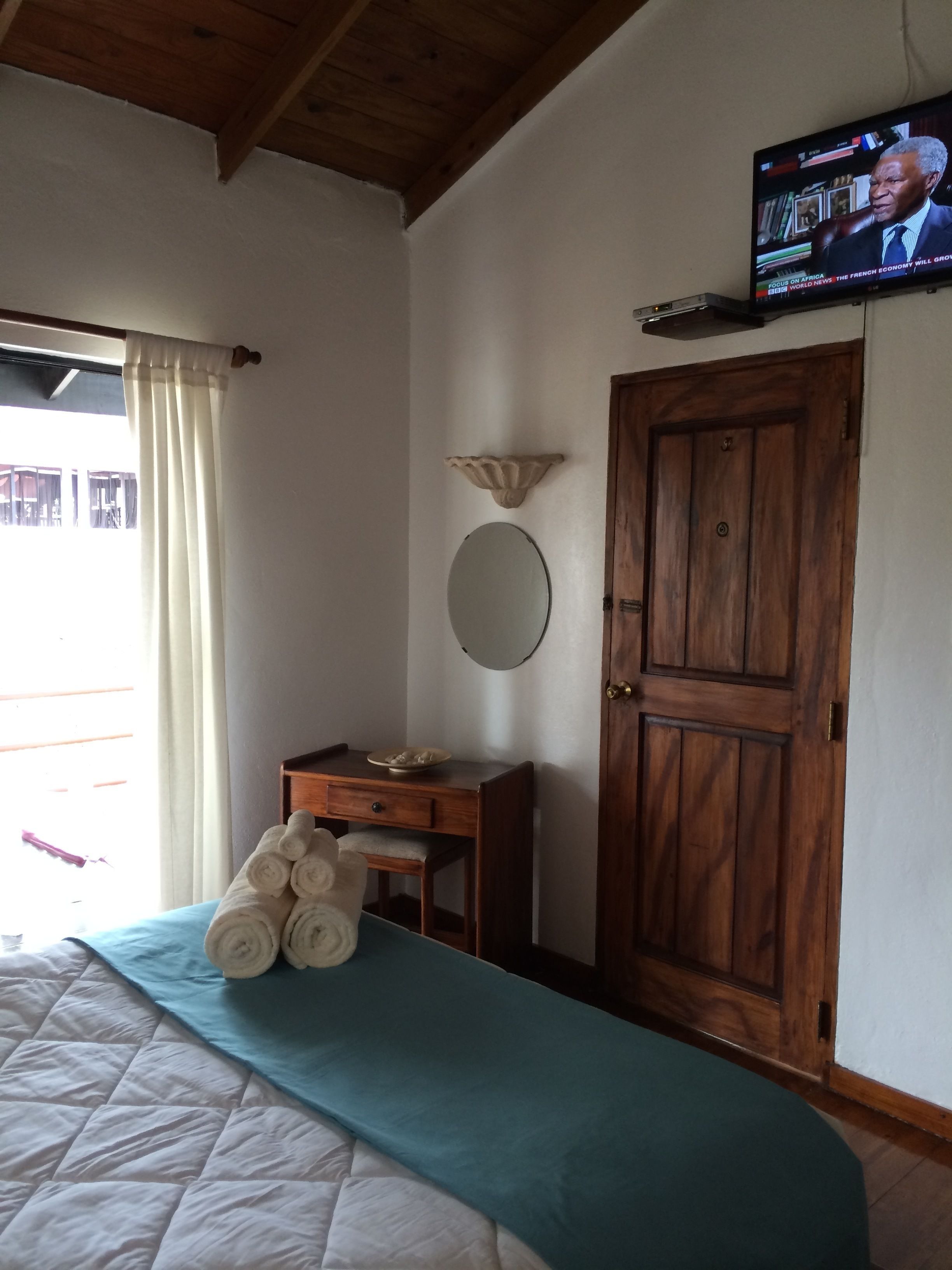 Un dormitorio con una cama, un aparador de madera, un televisor en la pared y una puerta.