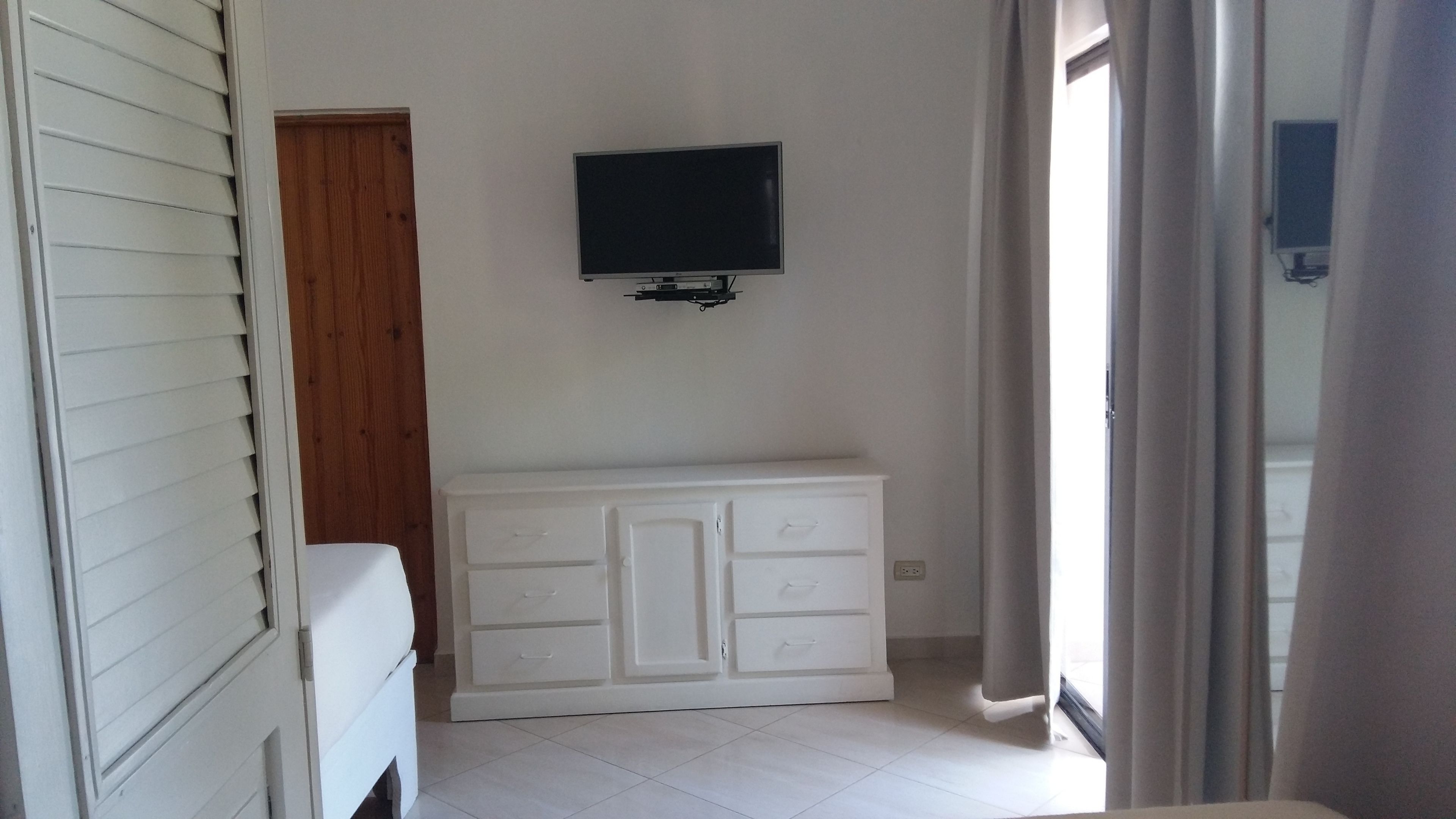 A room with a white cabinet, a television mounted on the wall, and a door leading to another room.