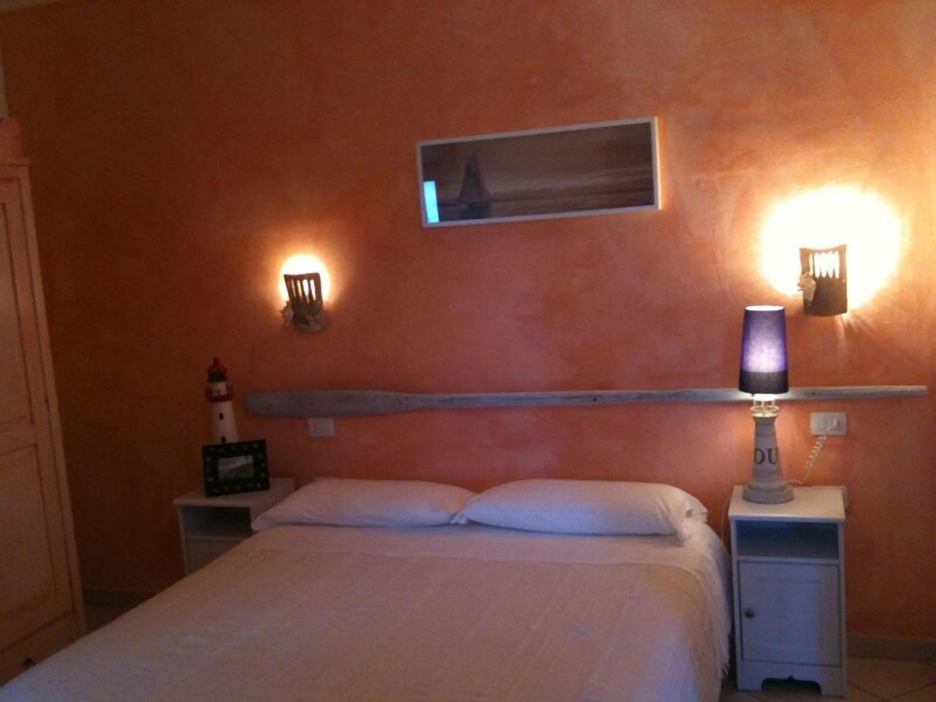 Une chambre à coucher comprenant un lit, deux tables de chevet, une étagère fixée au mur et deux appliques murales.