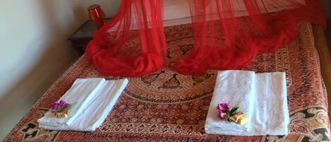 A bed with a red canopy, two towels with flowers, and a patterned rug.