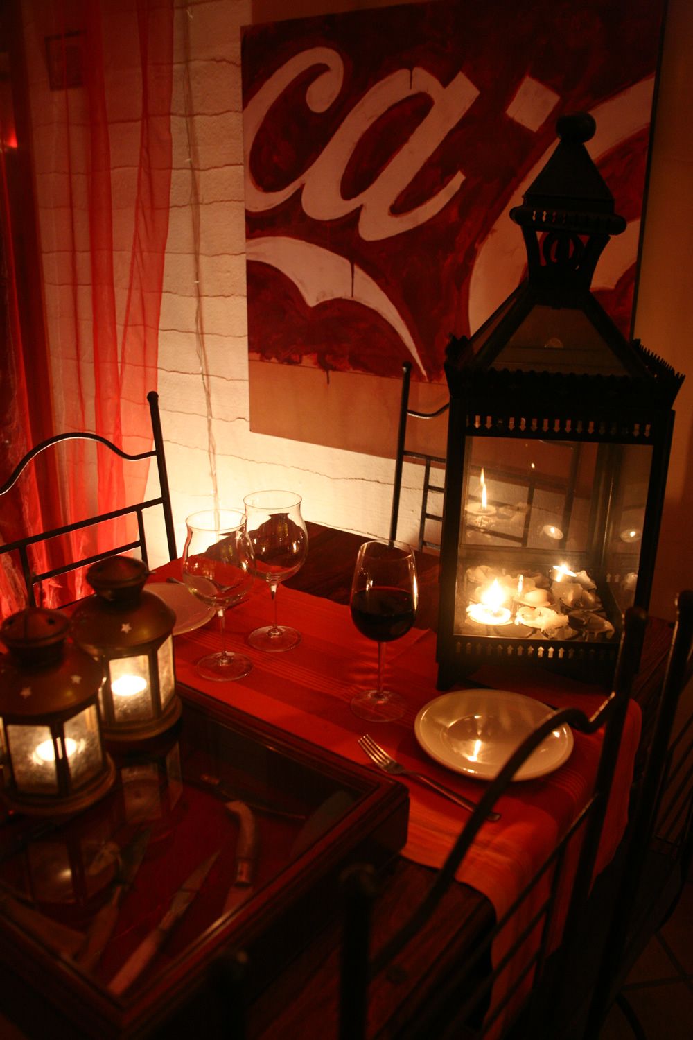 Une salle à manger à la lumière tamisée, avec une table dressée pour deux personnes, agrémentée de bougies, de verres à vin et d’une lanterne.
