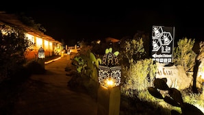 A nighttime view of a pathway leading to a building with illuminated lanterns and a sign indicating a reception and restaurant. - AgriRistoChic Resort Li Espi (Palau)