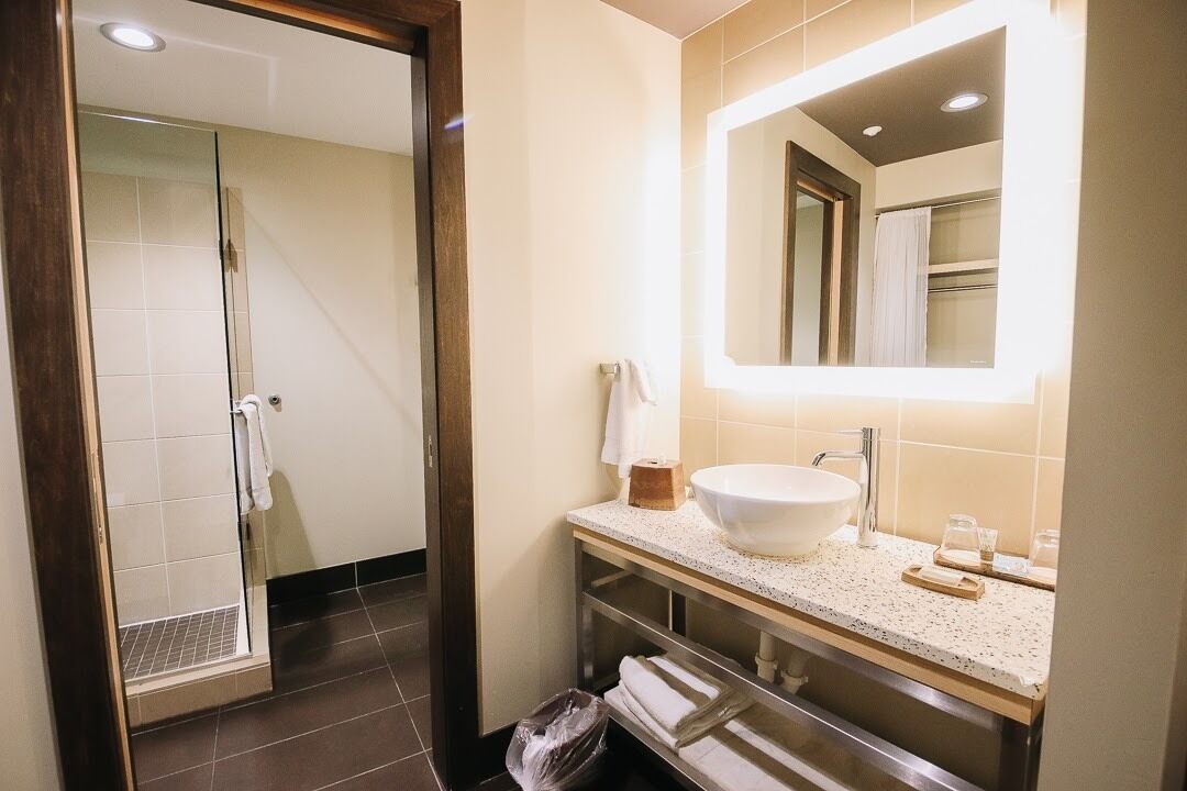 A modern bathroom with a glass shower door, a large mirror, a white sink, and a towel rack.