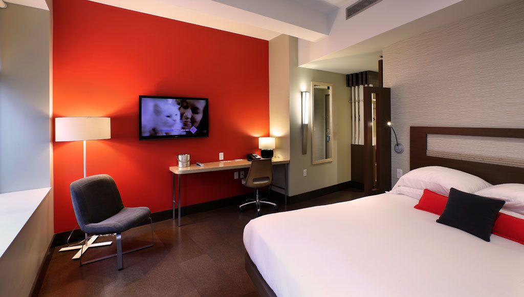 A hotel room with a bed, a desk, a chair, a TV, and a mirror.