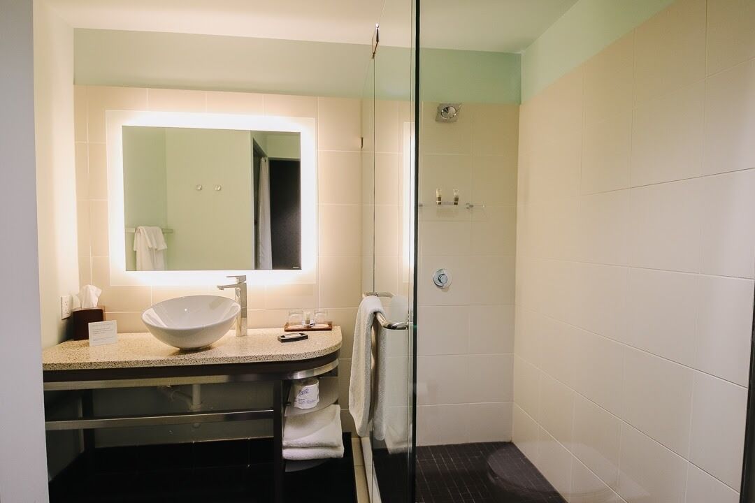 A bathroom with a large mirror, a round sink, a glass shower enclosure, and a towel rack.