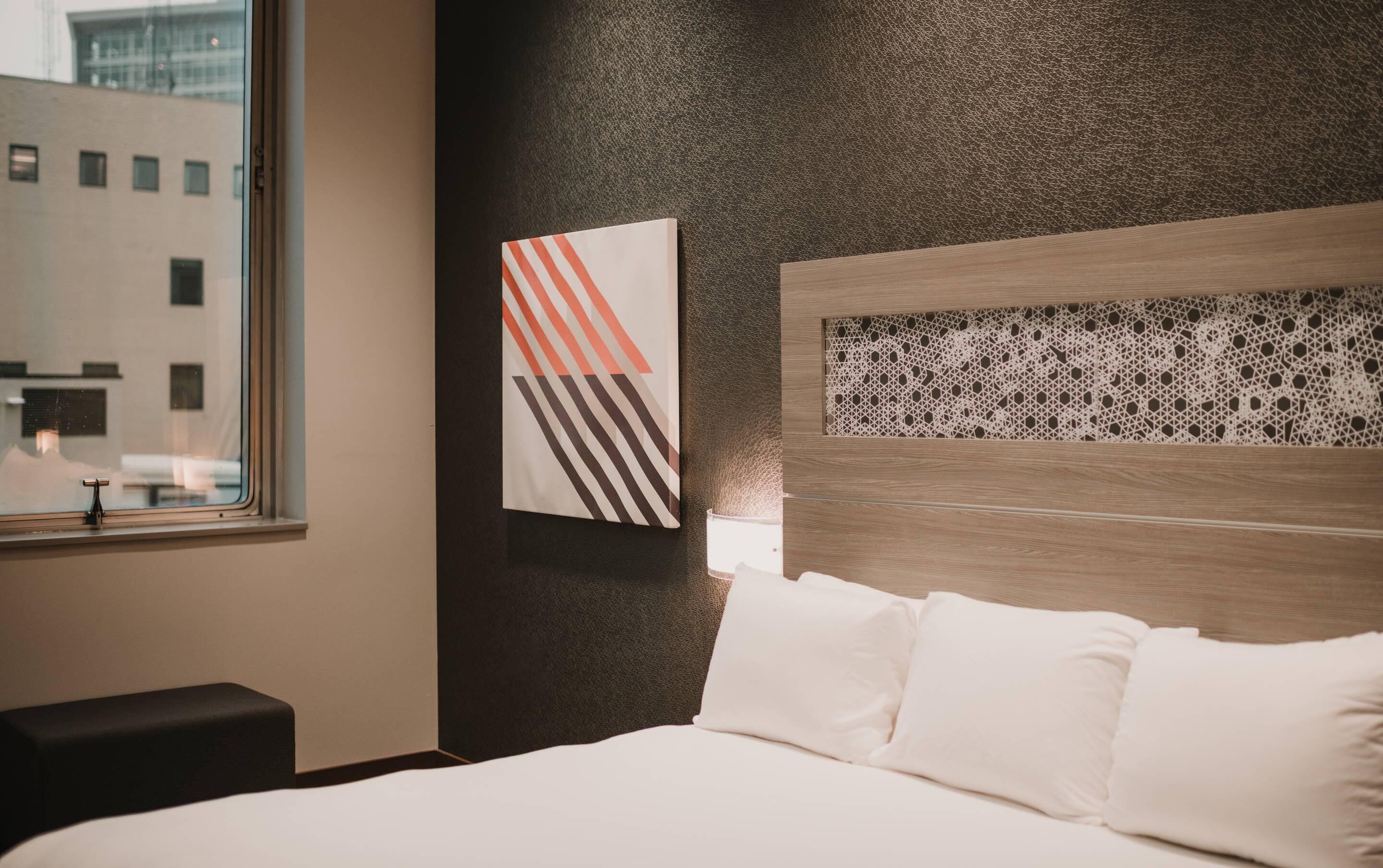 Une chambre d’hôtel avec un lit, une fenêtre et une œuvre d’art accrochée au mur.