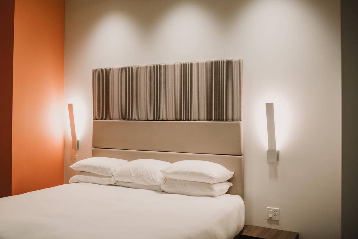 Ein modernes Hotelzimmer mit einem großen Bett, einem gestreiften Kopfteil und zwei Wandleuchten.