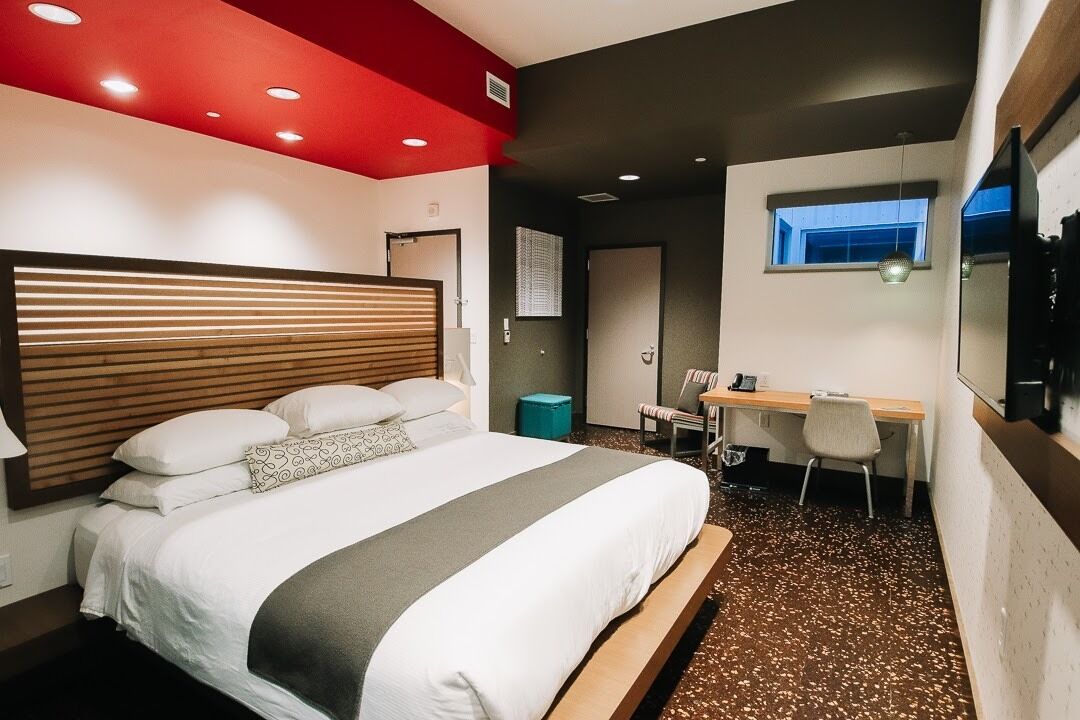 Una habitación de hotel moderna con una cama grande, un escritorio y un ventanal pequeño.