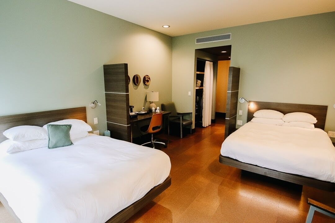 A hotel room with two beds, a desk, a chair, and a wardrobe.
