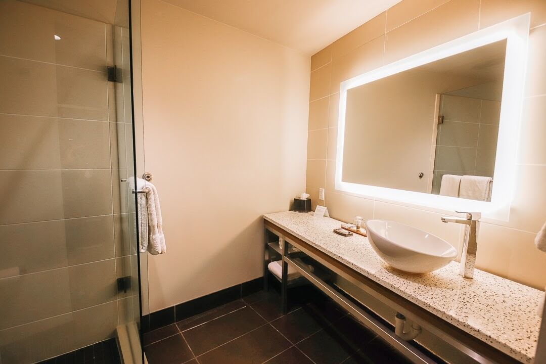 Een moderne badkamer met een douchecabine van glas, een wit wastafelmeubel met een grote spiegel en een aanrecht met een zeepbakje en een handdoek.