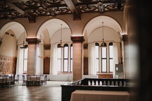 A spacious hall with high arched ceilings, large windows, and a marble floor.