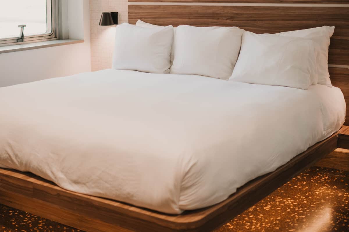 Ein ordentlich bezogenes Bett mit hölzernem Kopfteil in einem Hotelzimmer.