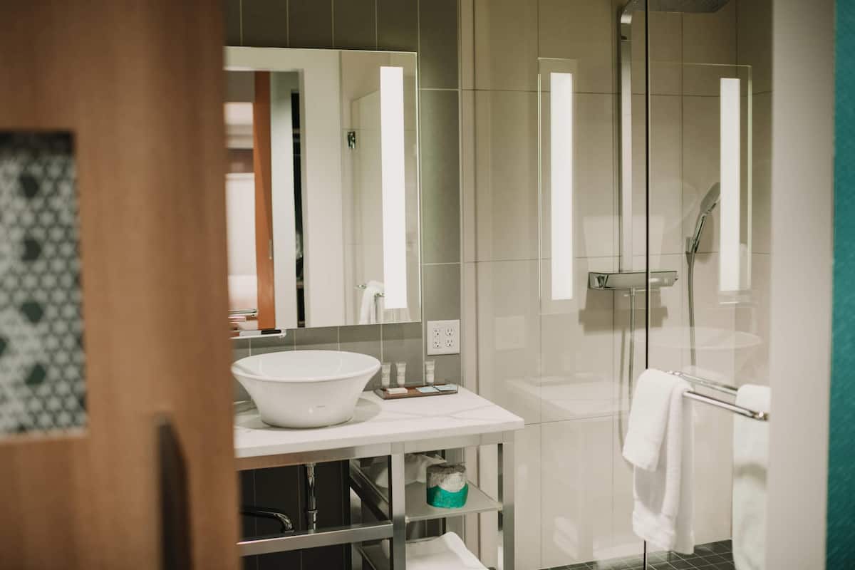 Ein modernes Badezimmer mit einem großen weißen Waschbecken, einer Duschkabine aus Glas und einem Spiegel über dem Waschbecken.