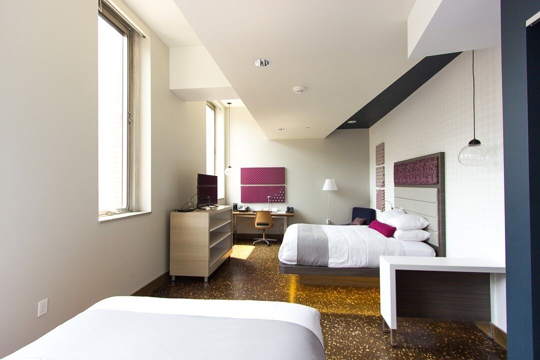 A modern hotel room with two beds, a desk, a chair, and a wardrobe.